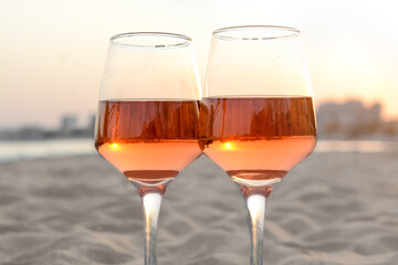 Glasses of tasty rose wine on sandy beach, closeup