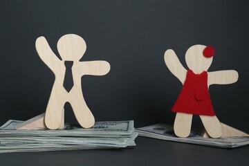 Gender pay gap. Wooden figures of man and woman on dollar banknotes against black background