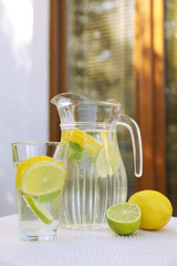 Water with lemons and limes on white table outdoors