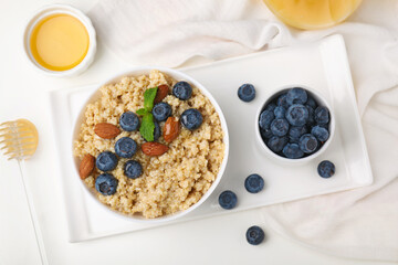 Bowl of delicious cooked quinoa with almonds and blueberries on white table, flat lay
