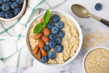 Bowl of delicious cooked quinoa with almonds and blueberries on white marble table, flat lay