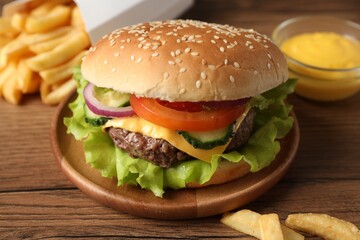 Delicious burger, sauce and french fries served on wooden table, closeup