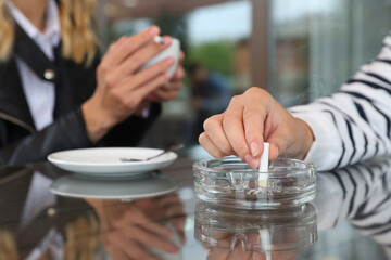 Woman putting out cigarette in ashtray at table, closeup