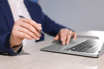Woman with pen working on laptop at wooden table, closeup. Electronic document management