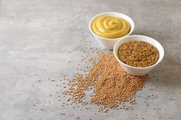 Bowls with mustard and seeds on grey table, space for text