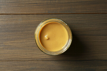 Spicy mustard in glass jar on wooden table, top view
