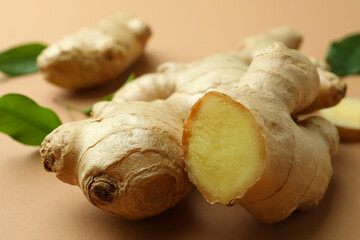 Fresh ginger and green leaves on light pale brown background, closeup