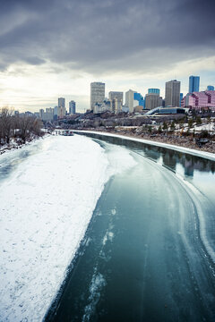 Winter City Skyline with half frozen river flowing under bridge on a cold snowy day