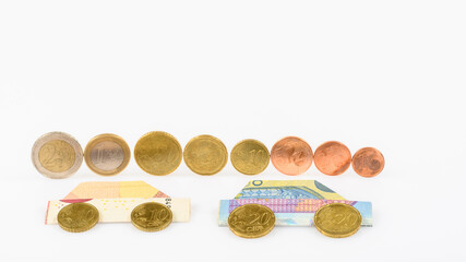 complete set of euro coins standing upright on a white table top and 2 cars folded from banknotes in front of it