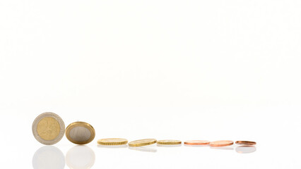 complete set of euro coins falls over on a white table - 2 euro coin still standing - with reflections