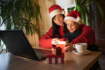 Happy family mom and son unpacking christmas gift from dad while sitting at home using laptop. Christmas concept