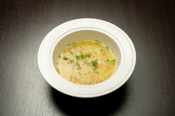 Vegan noodles soup with greens and vegetables served with thyme, light wooden background.