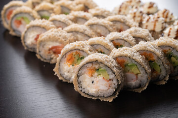 Tempura maki roll on black background. Hot sushi set with salmon, crab and cucumber inside. Modern japanese menu