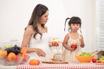 Mom with her two children eating fruits and vegetables. Mother with daughter having breakfast at home. Happy lifestyle family. Mother with her children in the kitchen cooking together.