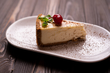 Delicious cheesecake, slice of New York style classical cheesecake on wooden background. Slice of tasty cake on white plate