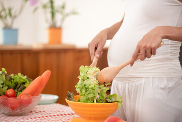 young pregnant woman makes herself salad of fresh vegetables, the concept of proper nutrition. high quality photo. pregnant woman in kitchen making salad.