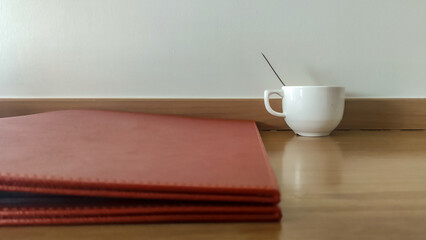 Fototapeta na wymiar White coffee cup and red folder. Blurred foreground.