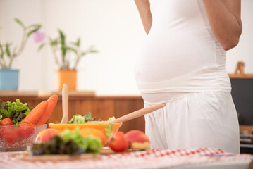 Obraz na płótnie Canvas young pregnant woman makes herself salad of fresh vegetables, the concept of proper nutrition. high quality photo. pregnant woman in kitchen making salad.
