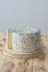 Round blue cheese wheel with cutted out piece on wooden cutting board on light background, selective focus