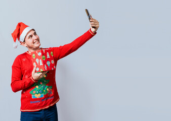 Fototapeta na wymiar Christmas handsome man taking a selfie holding a gift isolated. Happy guy taking a christmas selfie isolated, Smiling young man in christmas hat holding a gift and taking a selfie isolated