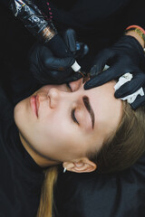 Beautician hand doing brow permanent makeup on an attractive female face - obrazy, fototapety, plakaty
