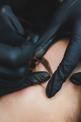 Fototapeta premium Beautician hand doing brow permanent makeup on an attractive female face