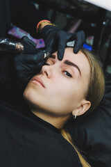 Fototapeta na wymiar Beautician hand doing brow permanent makeup on an attractive female face