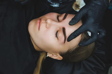 Beautician hand doing brow permanent makeup on an attractive female face - obrazy, fototapety, plakaty