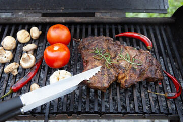 Beef steaks cooking on the charcoal grill with chili pepper, tomatoes, garlic and mushrooms for bbq sauce. - 548429329