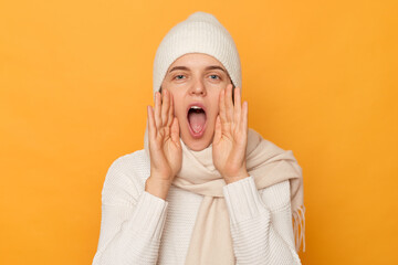 Listen me please. Attractive woman wearing warm clothes posing isolated over yellow background, shouting or exclaiming loudly, attracting somebody`s attention, keeps mouth widely opened.