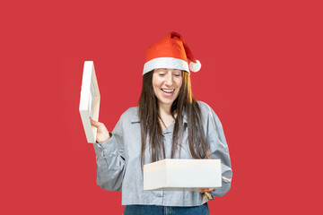 giovane ragazza con il cappello rosso di natale isolata con sfondo rosso felice di aprire una...