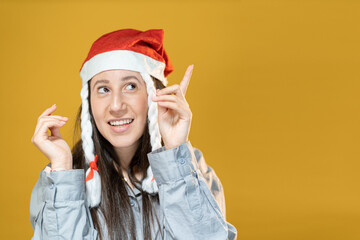 ragazza felice indossa cappello di natale alza l'indice verso l'alto indicando qualcosa, isolata con sfondo giallo.