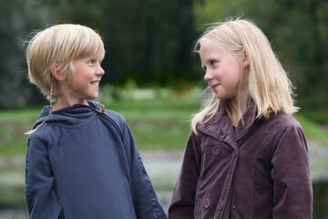Fototapeta premium Two blonde children little boy and girl are talking in the park outdoors