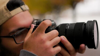 Close up of young male photographer raises up professional camera to take a photo