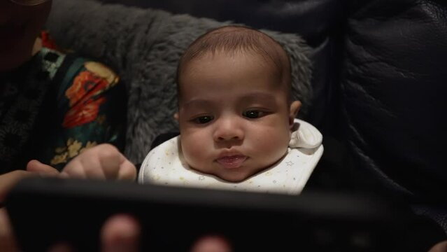 Adorable 2 Month Old Baby Boy Watching Smartphone held By Mother On Couch. Slow Motion, Close Up View Behind Phone