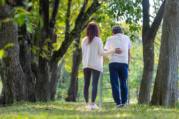 Asian senior father with walker and daughter walking together in the park during summer for light exercise and physical therapy usage