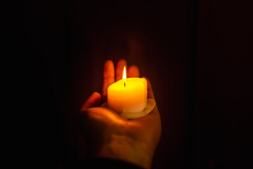 Burning candle in a mans hand at dark background.A man of prayer is praying, holding one burning candle.Religion concept.