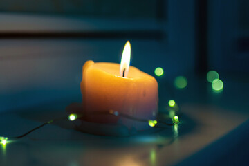 Burning candle with a small garland standing on a windowsill late in the evening night.poor...