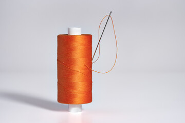 Spool of orange threads  with a needle on white background