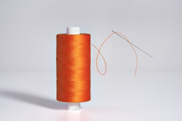 Spool of orange threads  with a needle levitate on white background