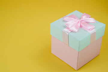 Pink and cyan gift box with ribbon bow isolated on yellow background