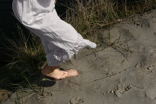 Close up lady feet on wet sand concept photo. White dress. Side view photography with windy weather on background. High quality picture for wallpaper, travel blog, magazine, article