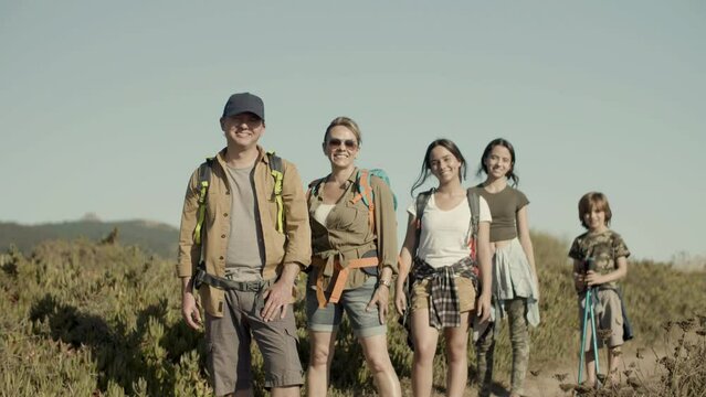 Caucasian family hiking on sunny day, standing in row, smiling. Parents and children posing on footpath, looking happy, enjoying hiking adventure on sunny day. Slow motion. Travel, family concept. 