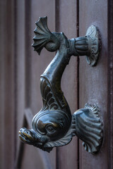 Closeup view of fish shaped vintage bronze door handle isolated on beautiful ancient brown wooden door, Montpellier, France