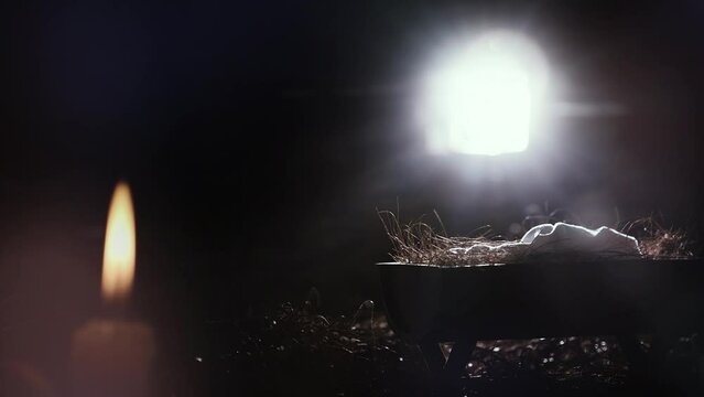 Bright light from the window illuminates the baby Jesus in the manger, Christmas and Christmas background, candle and candles celebrating the birth of Jesus Christ
