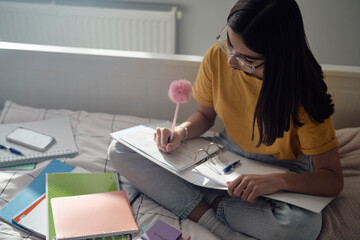 Caucasian teenage girl sitting on bed and learning from books