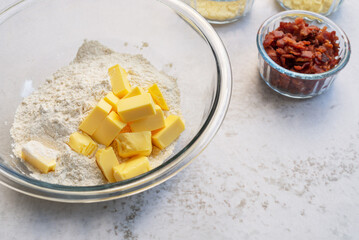 cold butter cube with flour, cheeses and bacon bits in glass bowl preparation for homemade savory scone on marble background