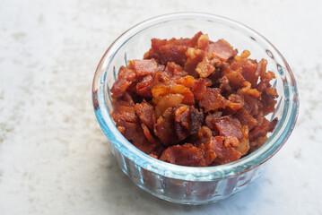 fried bacon bits in glass bowl on marble background
