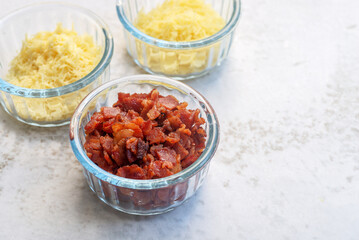 bacon bits, parmesan cheese and cheddar cheese in glass bowls on marble background