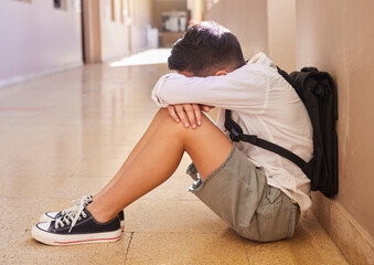 Anxiety, school and sad student bullying victim feeling depression, lost or stressed in hallway or corridor floor. Child, depressed boy or lonely male learner crying alone with abuse trauma or fear